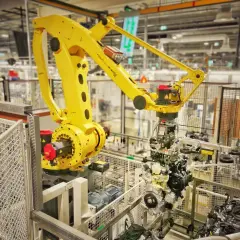 Żółty robot przemysłowy FANUC M-410iC pracuje nad montażem silnika, uosabiając filozofię kaizen toyota w nowoczesnej fabryce.
