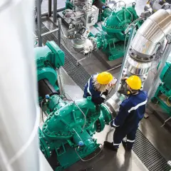 Dwóch inżynierów w żółtych kaskach sprawdza działanie pomp przemysłowych, dbając o oszczędzanie energii.