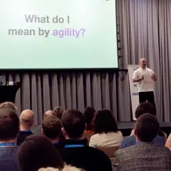 Prelegent wyjaśnia, co to agile, podczas konferencji. Na ekranie pytanie: "What do I mean by agility?".