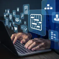 Dłonie pracują na laptopie, nad którym unoszą się ikony symbolizujące integrację systemów, zarządzanie projektami i współpracę.