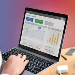 Osoba analizuje dane na laptopie, widoczne wykresy sprzedaży i globalnego rynku. Decyzje podejmowane są w sposób data driven.