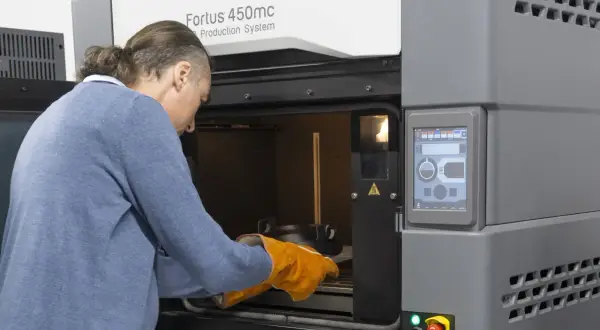 Mężczyzna w rękawicach zakłada element do drukarki 3D Fortus 450mc.