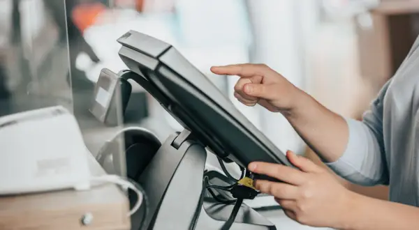 Dłoń dotyka ekranu terminala płatniczego. To jest właśnie point of sale, czyli miejsce sprzedaży.