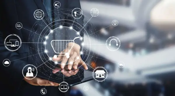 Biznesmen korzysta z tabletu, na którym wyświetla się grafika przedstawiająca koszyk zakupowy i ikony związane z e-commerce, takie jak drp ii.