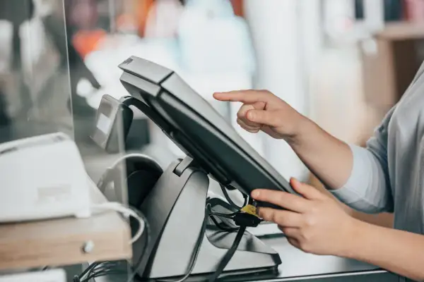 Dłoń dotyka ekranu terminala płatniczego. To jest właśnie point of sale, czyli miejsce sprzedaży.